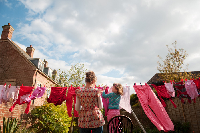 woman and girl hanging pink and red laundry on a clothesline together with blue skies above in england