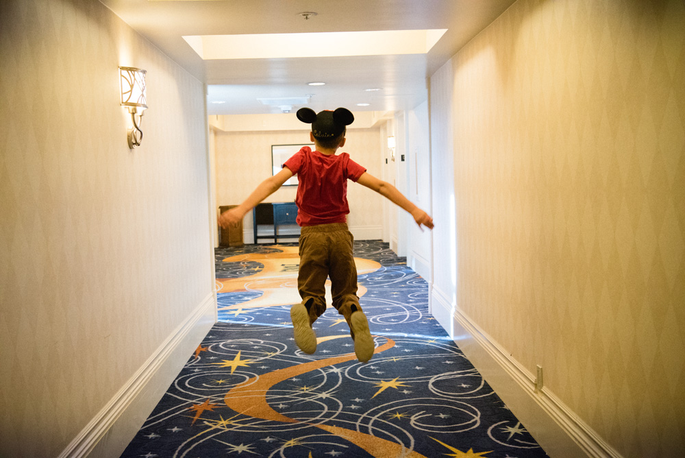 young boy jumping in hallway wearing a mickey mouse ears hat