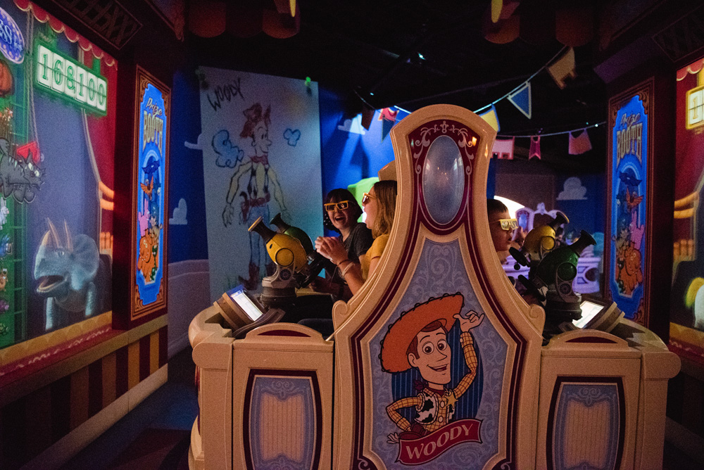 two girls and laughing on a toy story ride with a rhino on a screen and another boy