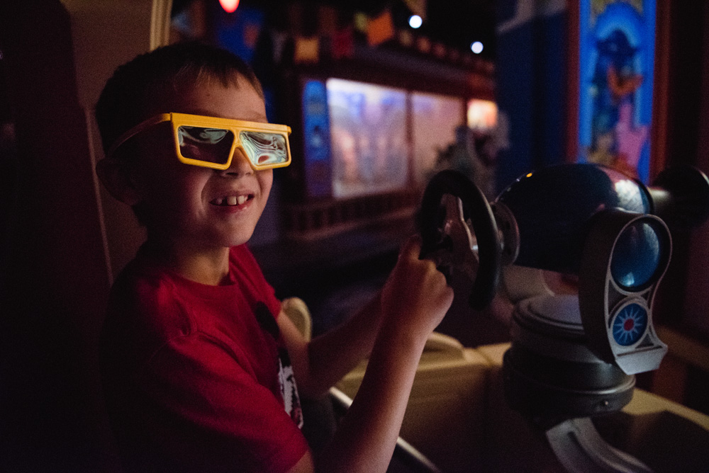 young boy with 3-d glasses on his face wearing a red shirt in an amusement park