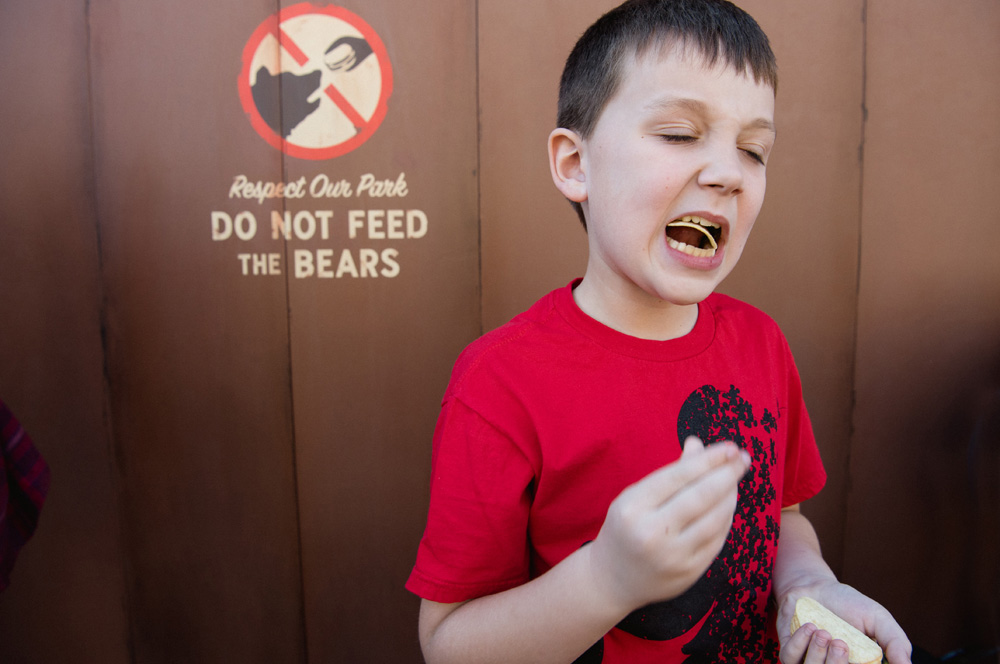 a boy eating a chip with a do not feed the bears sign on a wall