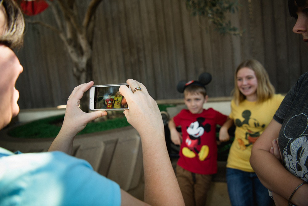 woman taking a photo on her iphone of two kids wearing mickey mouse shirts