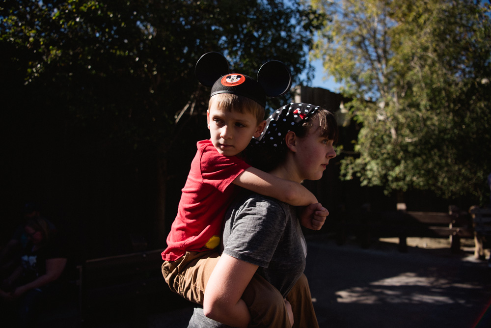 a girl carrying a boy on her back who is wearing a mickey mouse ears hat