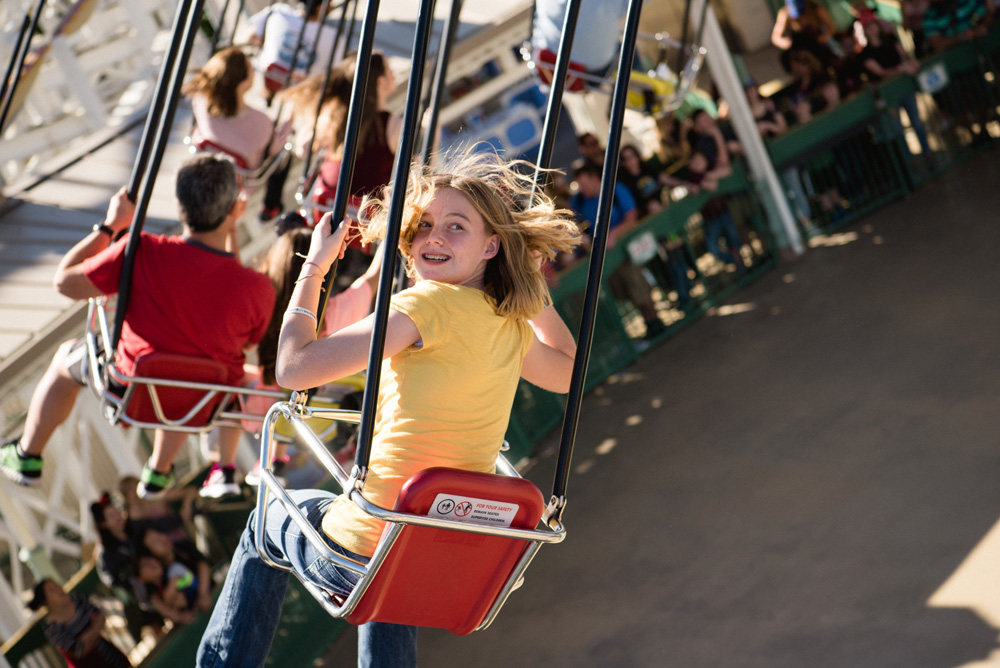 a teenage girl in a yellow shirt riding on an amusement park swing