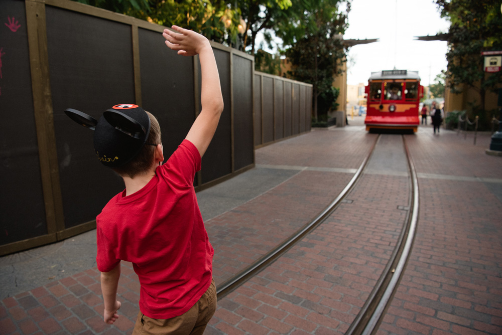 a boy in a red shirt waving to a red trolley